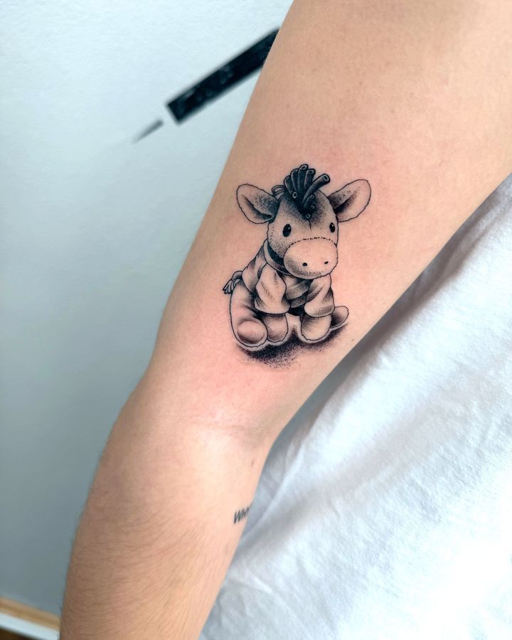 Kleines Black-and-Grey-Tattoo eines Plüschesels auf dem Oberarm