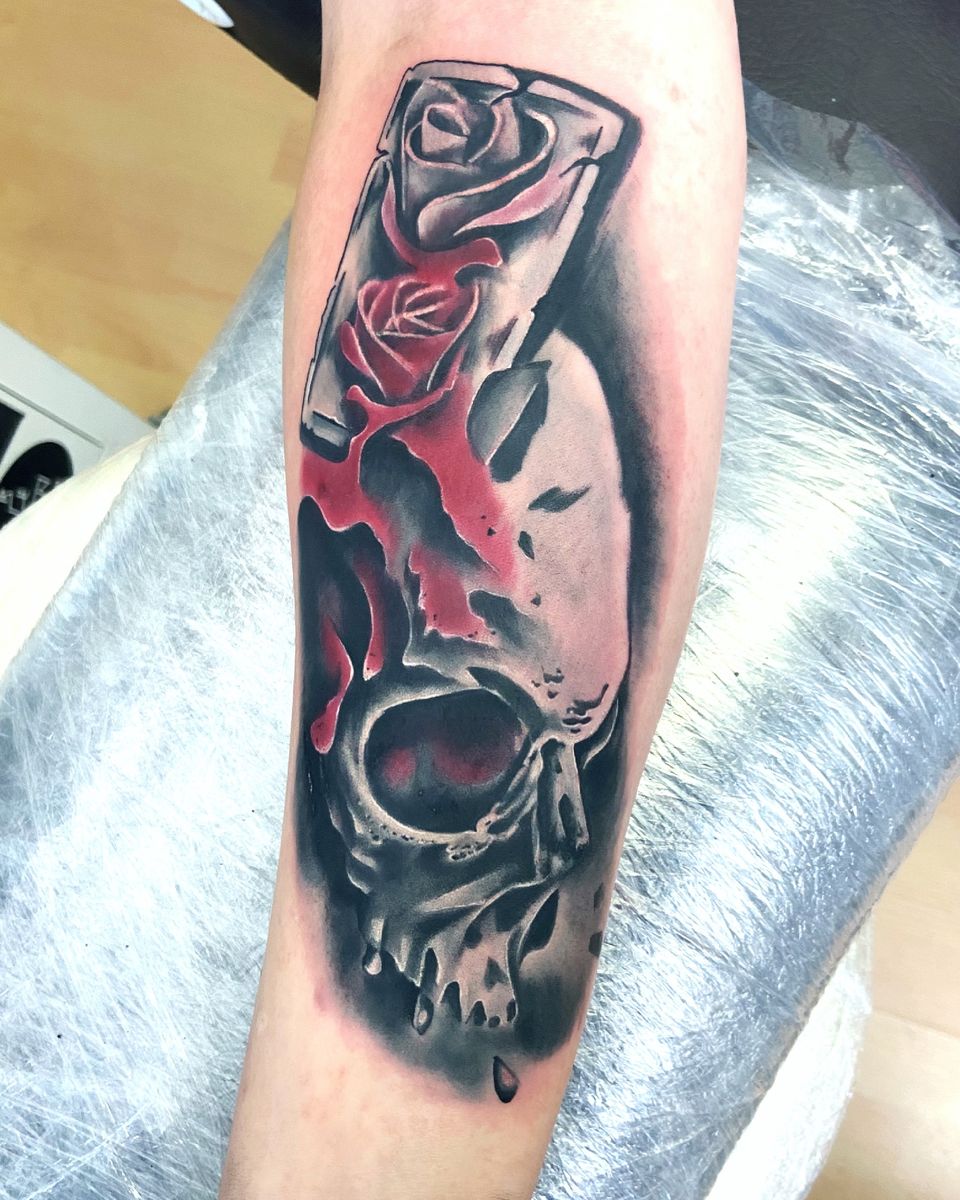 Trash-Polka-Tattoo mit roten Rosen in einem Rahmen über einem Schädel in Schwarz auf dem Unterarm
