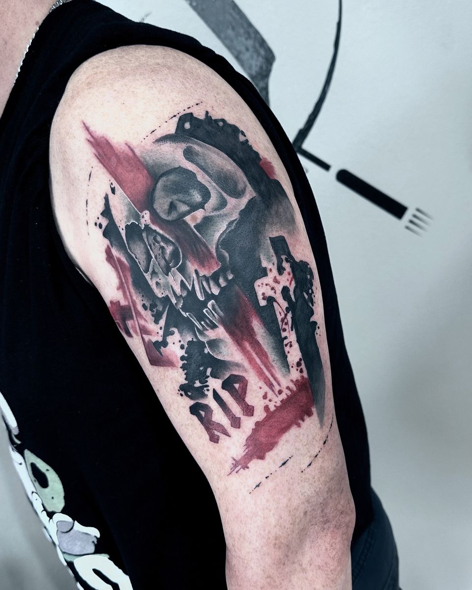 Trash-Polka-Tattoo eines Schädels mit Grabkreuz, roten Pinselflächen und Schriftzug RIP auf dem Oberarm